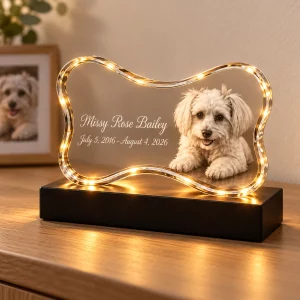 Bone-shaped pet memorial crystal lamp displayed on a sideboard with a blurred dog photo nearby