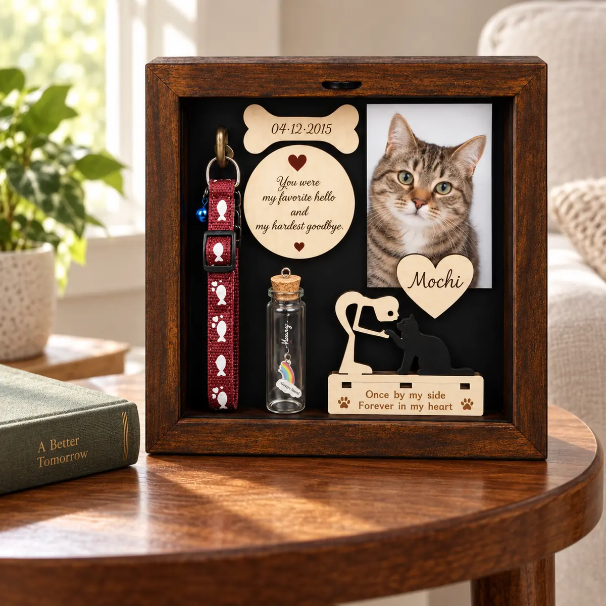 Cat memorial shadow box on an indoor side table beside a book