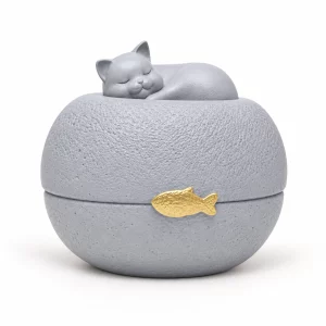 Sleeping cat sculpture resting on a round gray pet urn with gold fish accent